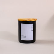 Black amaraa soy wax candle with wooden lid and white label on neutral background